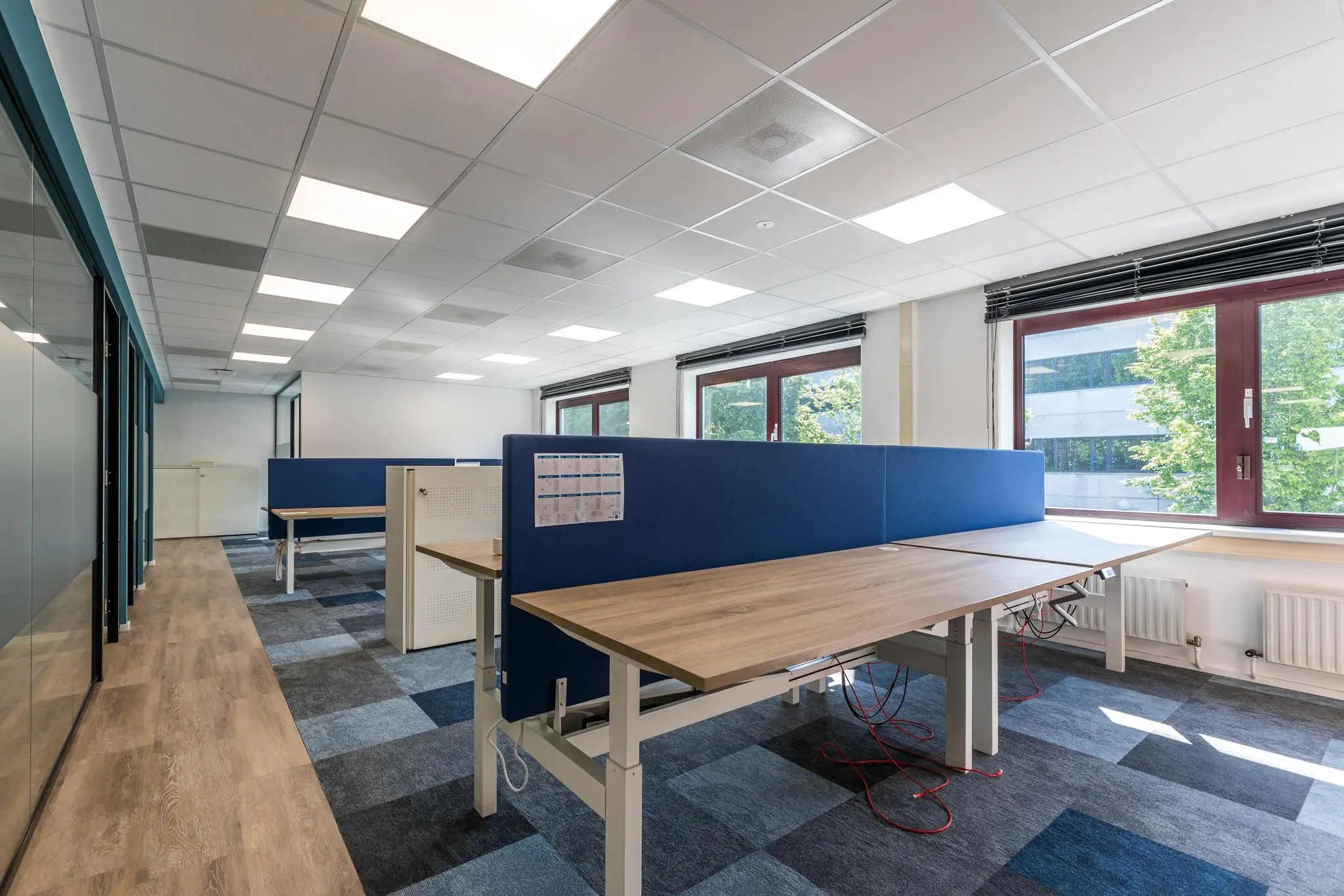 Moderne, open kantooruimte aan de Baarnsche Dijk met verstelbare bureaus, blauwe scheidingswanden en grote ramen.